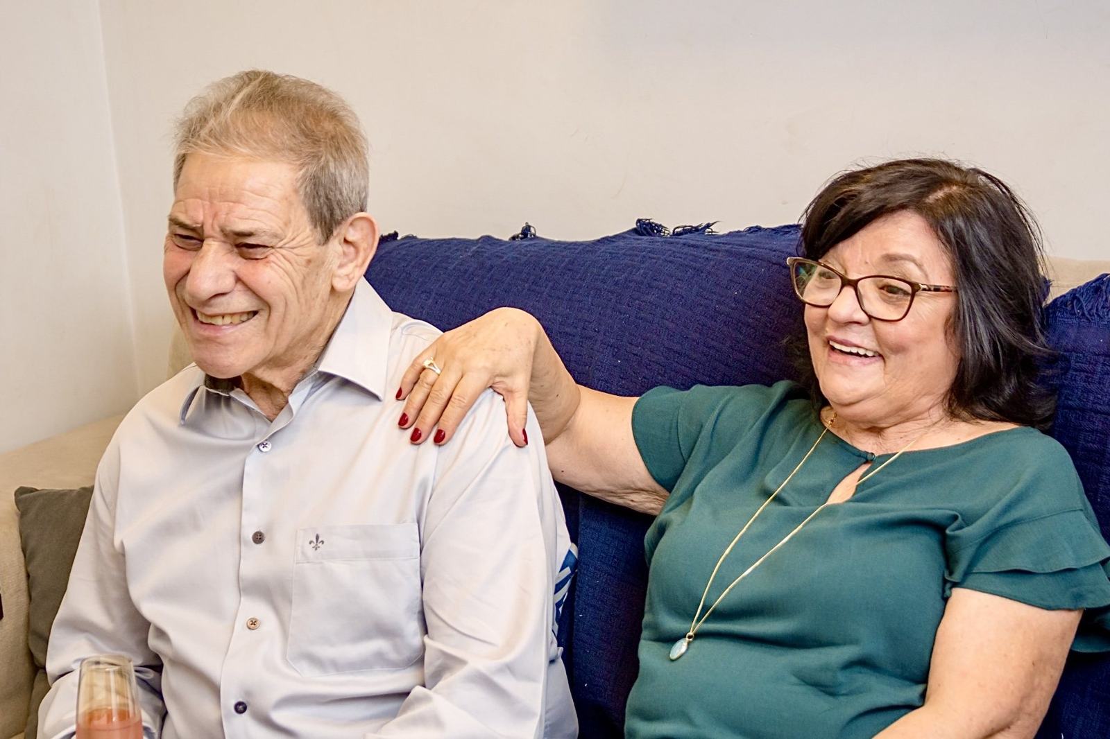 Silvio rindo no sofá, com a esposa de mão no seu ombro